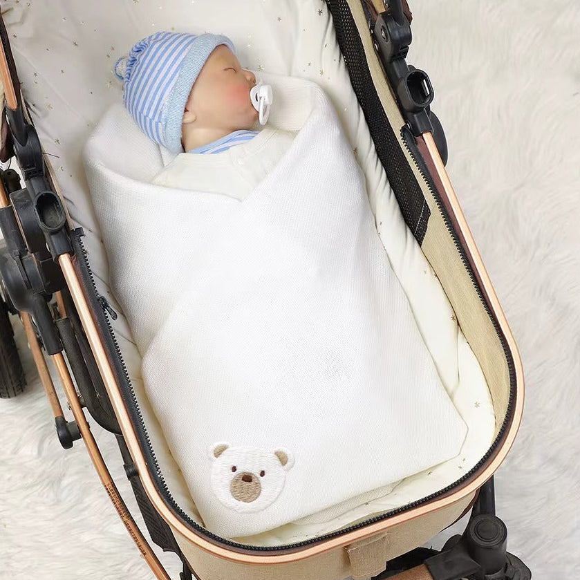Newborn baby wrapped in a blanket with a teddy bear design, lying in a stroller.