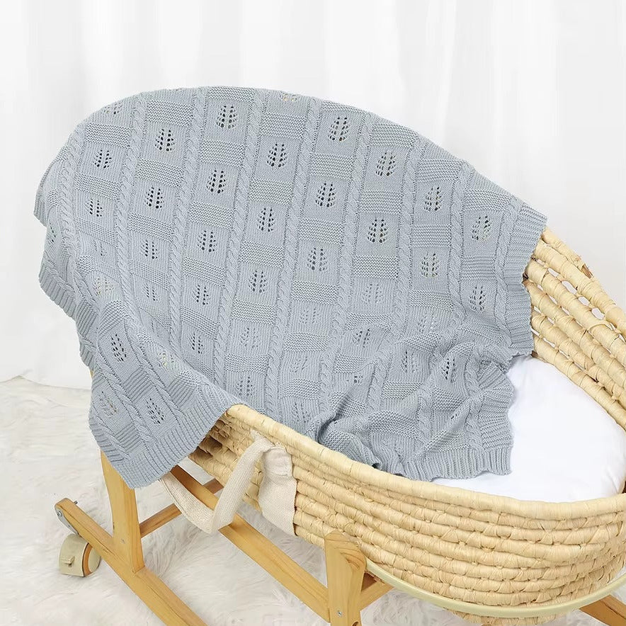 Gray textured blanket draped over a wooden Moses basket on a white background
