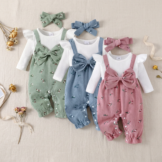 Three cottagecore floral corduroy baby overall rompers in sage green, slate blue, and dusty pink, laid flat with their matching headbands.