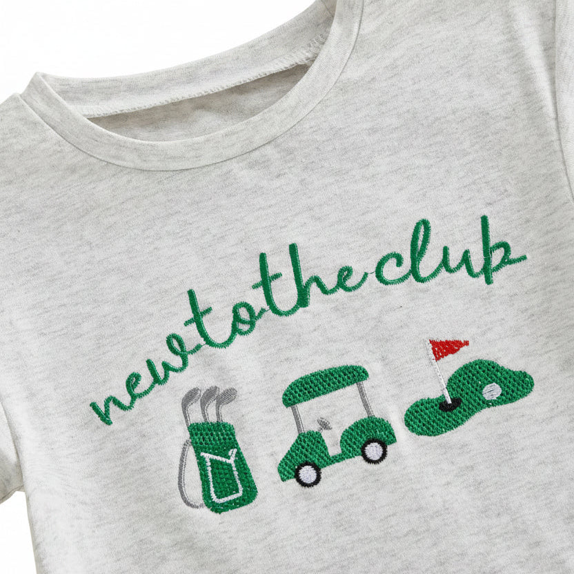 Close-up detail of the "new to the club" chest graphic featuring a golf bag, golf cart, and flag on the grey baby romper.