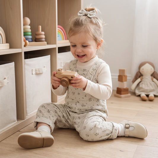 Toddler girl sitting on the floor wearing a vintage-inspired floral corduroy jumpsuit and long sleeve shirt