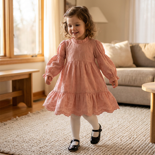 Toddler girl smiling and running indoors while wearing a pink floral embroidered long sleeve dress with white tights.