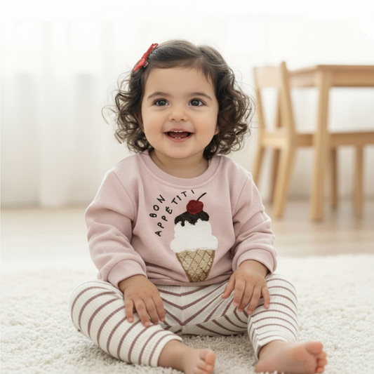 Toddler Girl wearing a pink sweatshirt with ice cream design and text, sitting on a light-colored floor.