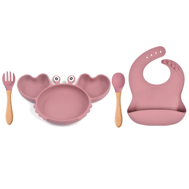 Pink children's dining set with plate, bowl, spoon, fork, and bib on a white background