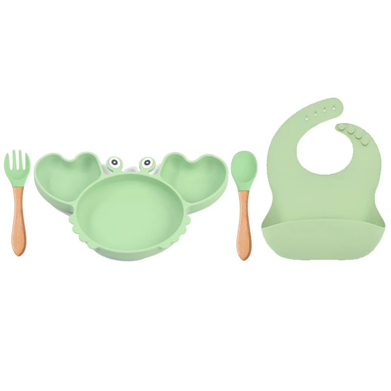 Set of green children's dining utensils including a bowl, spoon, fork, and bib on a white background.