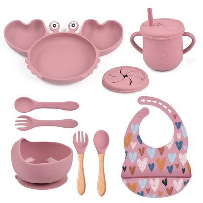 Pink children's dining set with plate, cup, bowl, utensils, and bib on a white background