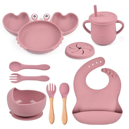 Pink children's dining set including plate, cup, bowls, utensils, and bib on a white background