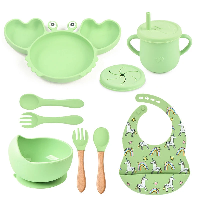 Green children's dining set including bowl, spoon, fork, cup, and bib on a white background