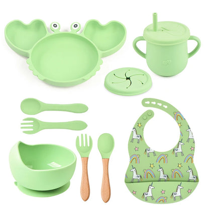 Green children's dining set including bowl, spoon, fork, cup, and bib on a white background