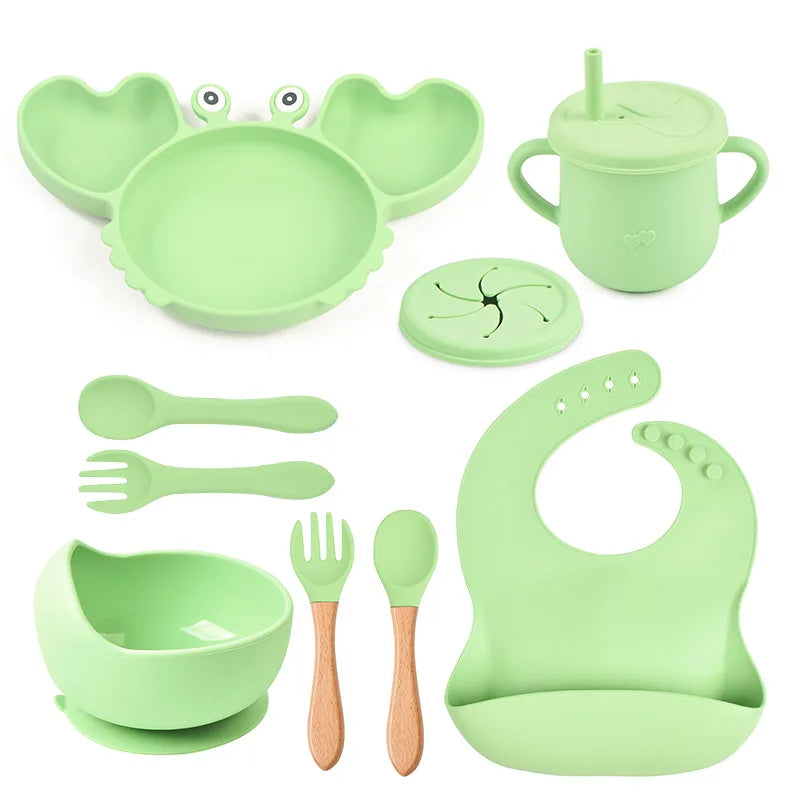 Green baby dining set including plate, cup, bowl, utensils, and bib on a white background