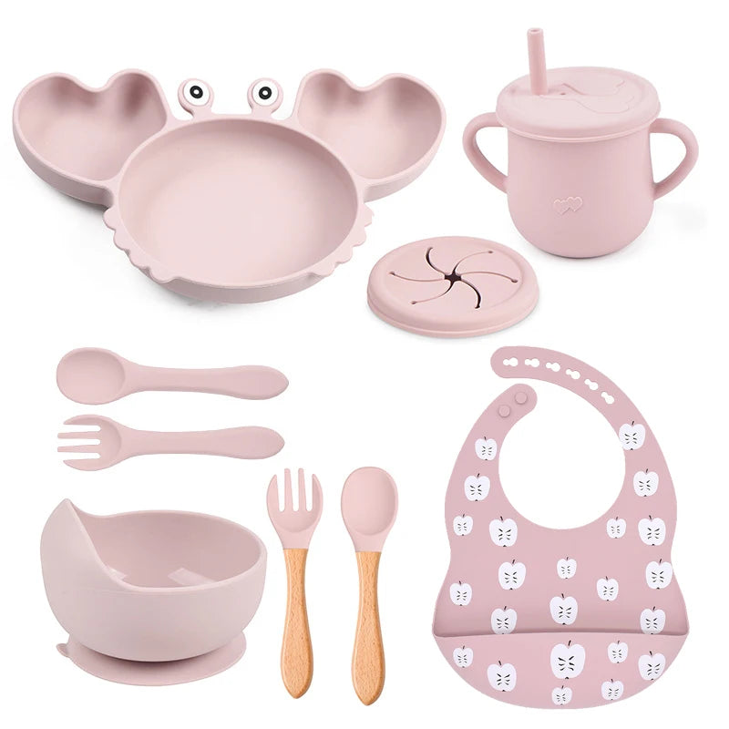 Pink children's dining set including plate, bowl, cup, utensils, and bib on a white background