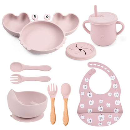 Pink children's dining set including plate, bowl, cup, utensils, and bib on a white background