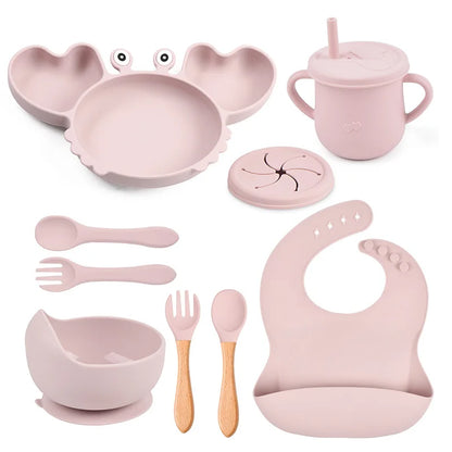 Pink baby dining set including bowl, spoon, fork, cup, and bib on a white background
