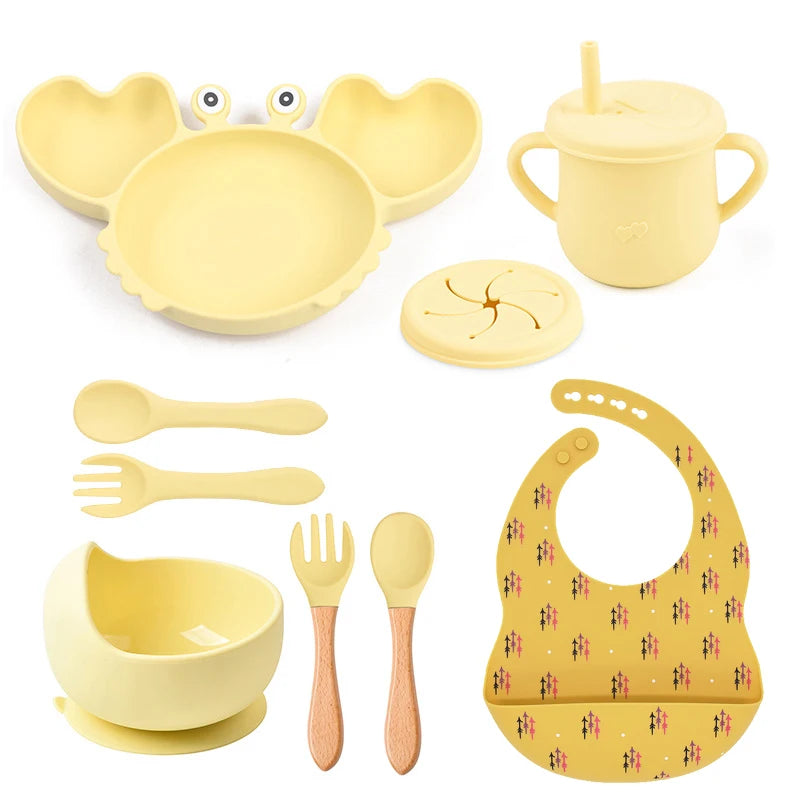 Yellow baby dining set including plate, cup, bowl, utensils, and bib on a white background