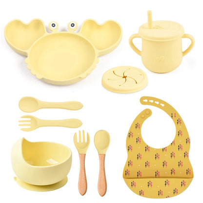 Yellow baby dining set including plate, cup, bowl, utensils, and bib on a white background