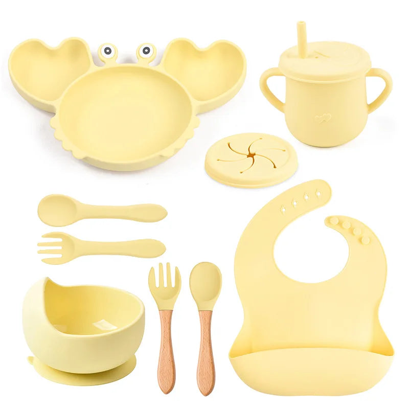 Yellow baby dining set including bowl, spoon, fork, cup, and bib on a white background