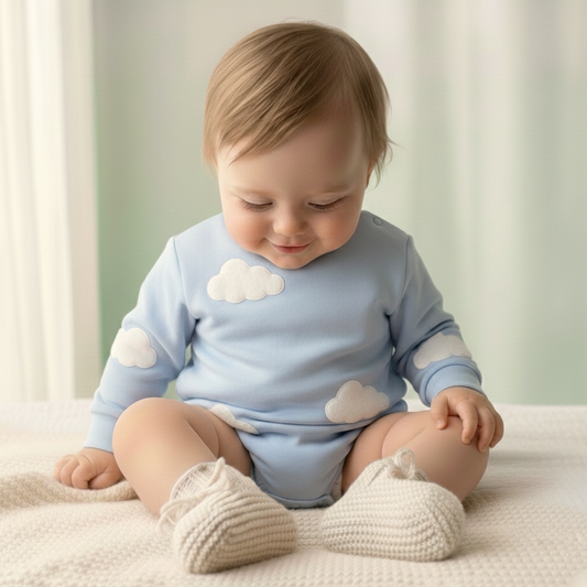 Baby wearing a light blue onesie with cloud patterns, sitting on a white blanket.
