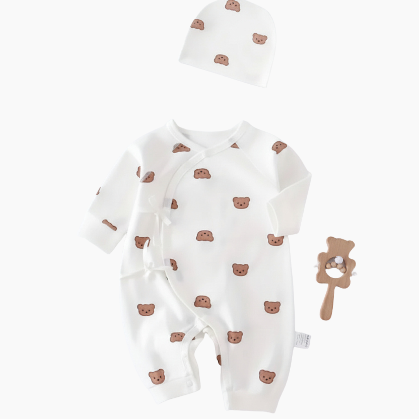 Baby romper with bear pattern and matching hat, accompanied by a wooden rattle on a white background.