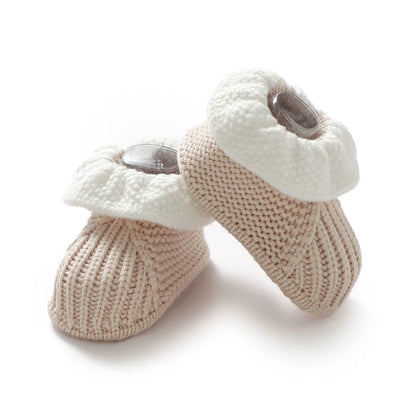 Pair of knitted baby booties with white tops and beige bodies on a white background