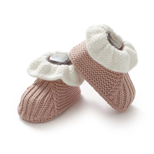 Pair of pink knitted baby booties with white scalloped edges on a white background