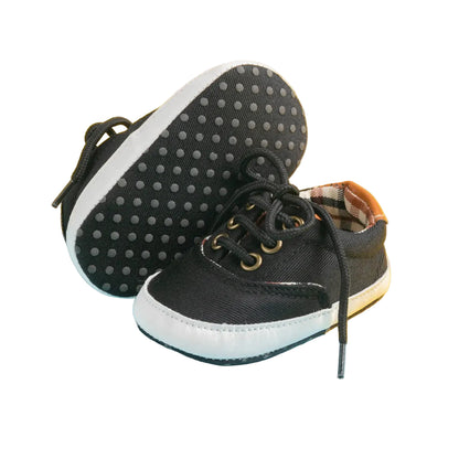 Black baby shoes with white soles on a yellow and blue background
