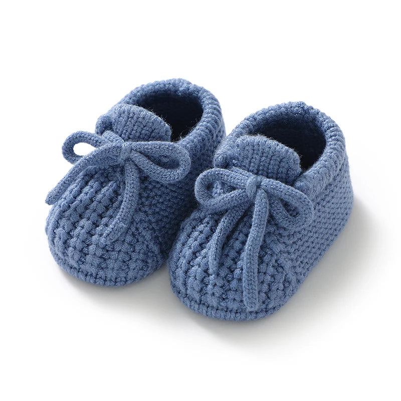 Pair of blue knitted baby shoes with bows on a white background