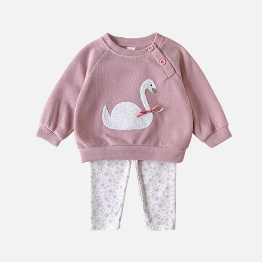 A two-piece baby girl outfit featuring a dusty pink long-sleeve sweatshirt with a white swan appliqué and floral print leggings on a white background