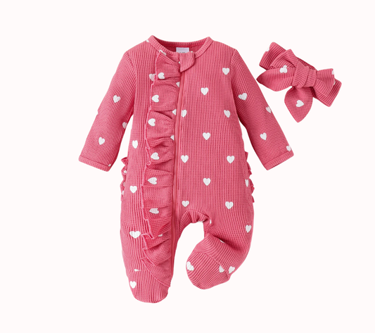 Deep pink waffle knit baby girl romper with white heart print, named Raspberry Sorbet. Features ruffled zipper detail, footed bottoms, and a matching bow headband.