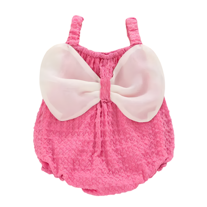 Back of pink baby girl romper showing oversized white chiffon bow creating a butterfly wing silhouette.