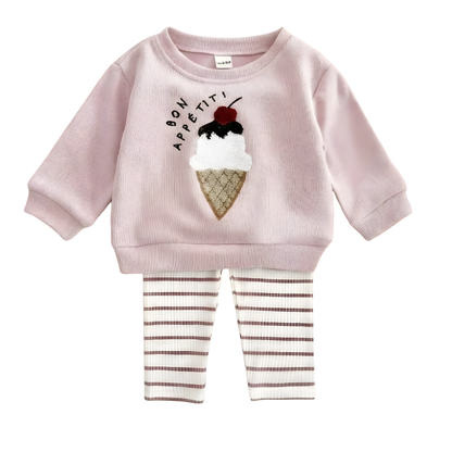 Flat lay view of baby girl two-piece outfit set including a pink long-sleeve pullover with textured ice cream cone design and "Bon Appétit" text, paired with coordinated striped ribbed leggings.