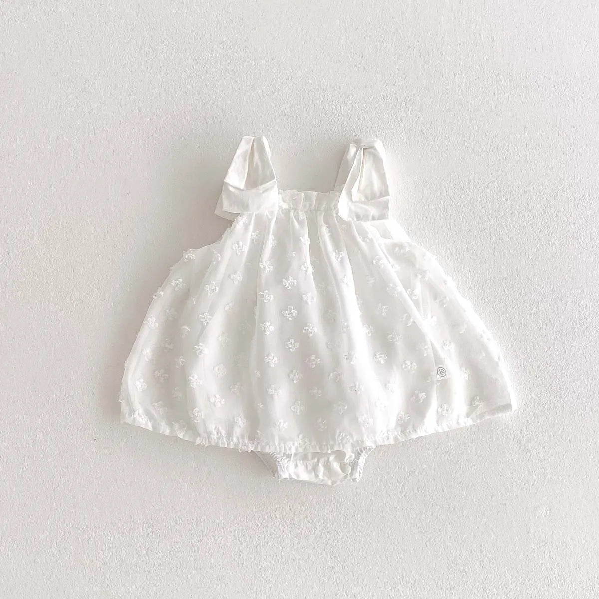 White baby dress with bow straps on a light gray background