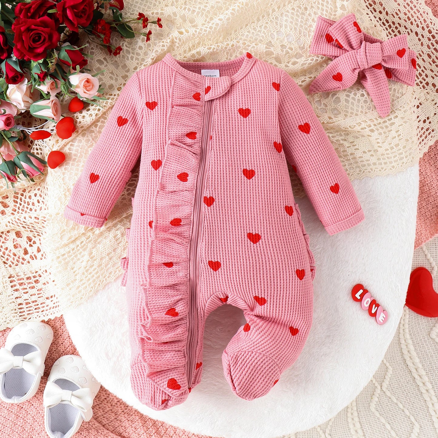 Pink waffle knit baby romper with red hearts, named Cherry Cordial. Perfect Valentine's Day outfit with ruffles, zipper closure, and matching hair bow.