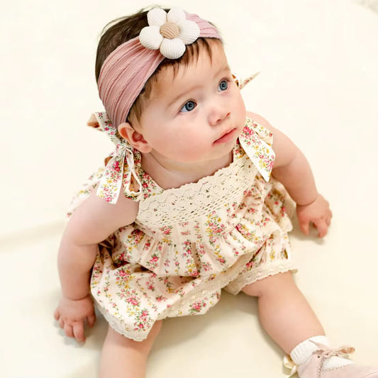 Baby wearing a dusty rose floral headband and floral dress on a white background