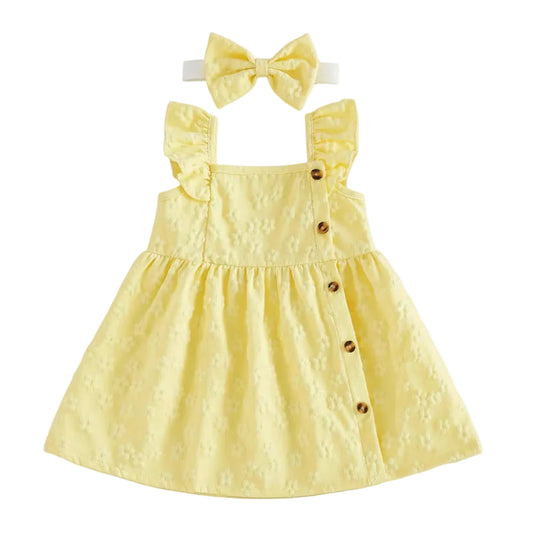 Flat lay of a baby girl's soft yellow sleeveless summer dress featuring a 3D floral embossed pattern, ruffle sleeves, and side buttons, including a matching yellow bow headband on a white background.