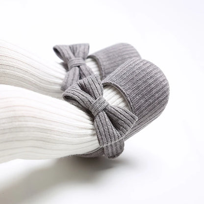 Baby wearing grey ribbed knit soft sole Mary Jane crib shoes with white ribbed tights.