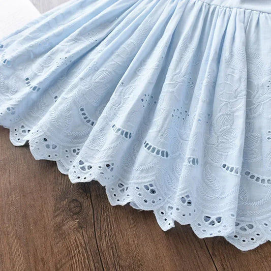 Close-up detail of premium 100% cotton Broderie Anglaise floral embroidery and a delicate scalloped eyelet hemline on a blue children's dress.