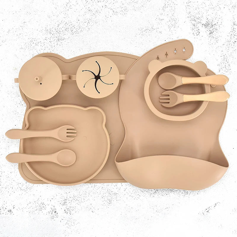 Khaki silicone placemat with cutlery and bib on a white background