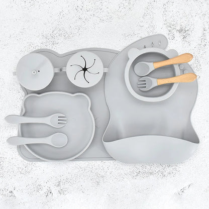 Grey 10-piece silicone baby feeding set displayed flat, featuring a divided suction plate, bowl, bib, straw cup, placemat, 2 spoons, and 2 forks.