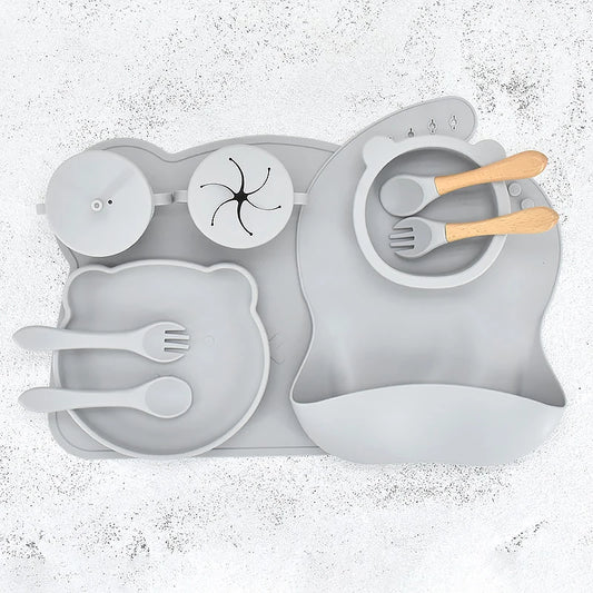 Grey 10-piece silicone baby feeding set displayed flat, featuring a divided suction plate, bowl, bib, straw cup, placemat, 2 spoons, and 2 forks.