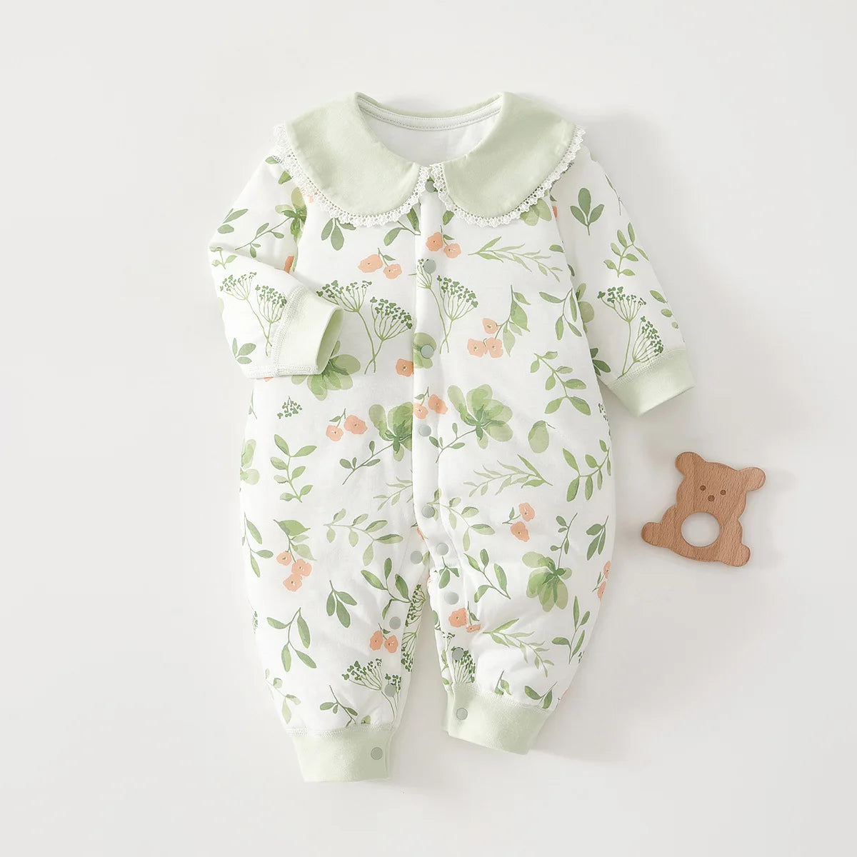 White long-sleeve baby jumpsuit with sage green botanical leaf and wildflower print, featuring a matching green collar with delicate white lace edging.