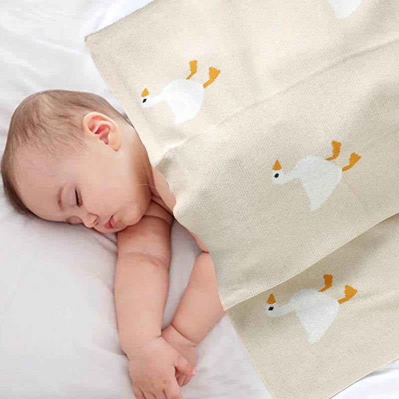 Baby sleeping under a blanket with goose designs on a white background