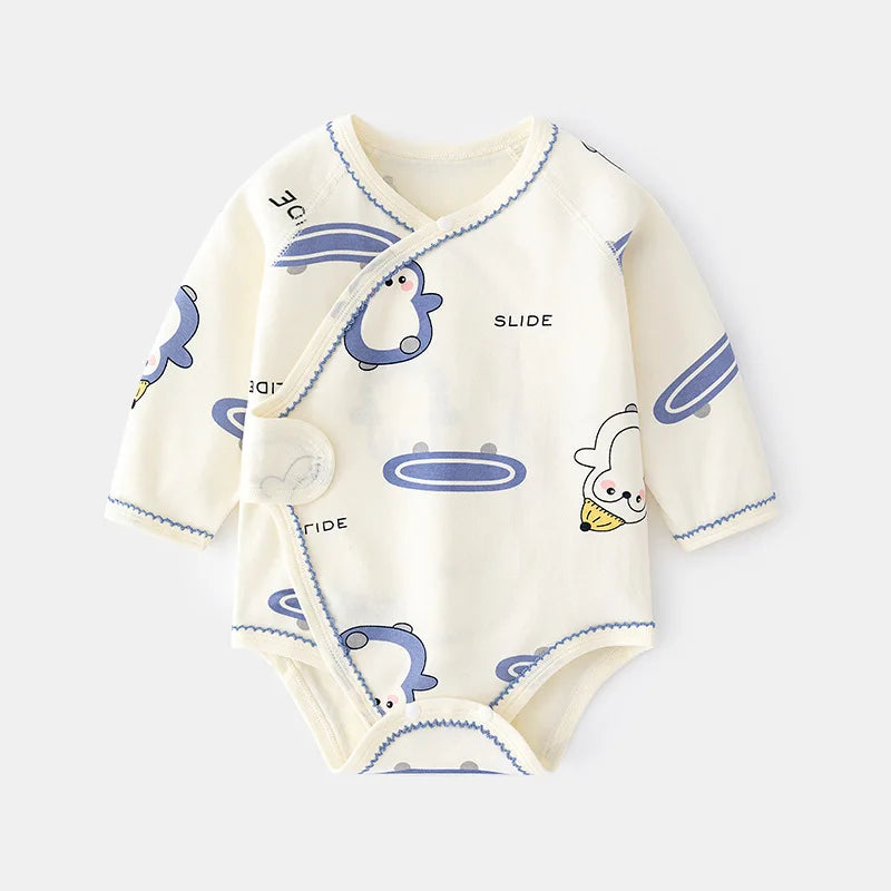 Side-snap baby bodysuit in cream with a playful blue penguin and slide print. Soft cotton wrap-over style.