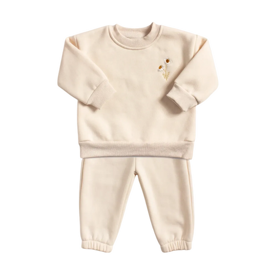 Flat lay of a cream two-piece baby lounge set, showing a crewneck sweatshirt with small daisy embroidery on the left chest and matching jogger pants