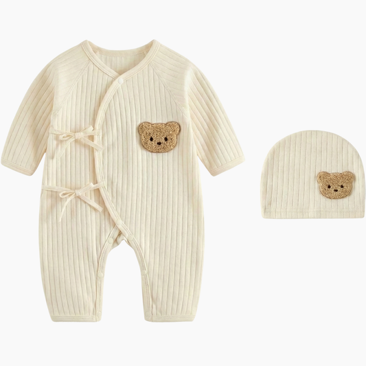 Cream colored ribbed cotton newborn jumpsuit with wrap-style front and textured beige teddy bear detail on chest and hat.