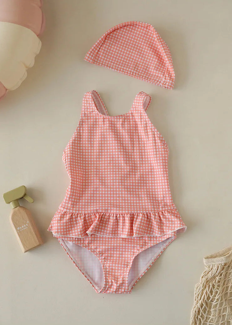 An Apricot Peach orange and white checkered one-piece swimsuit for toddlers, shown with a matching ruffled swim cap in a soft pastel palette.