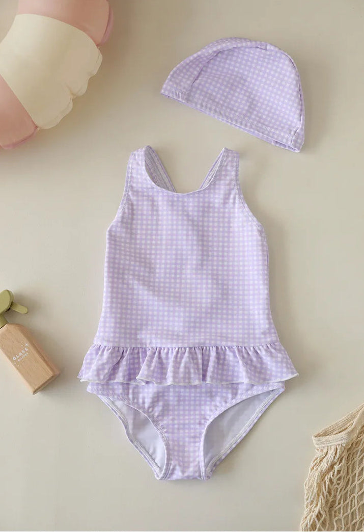 A Wildflower Lavender purple gingham swimsuit set for girls, including a backless one-piece with ruffle trim and a matching purple checkered swim hat.