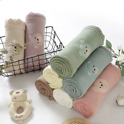 Set of rolled-up baby blankets with bear designs on a white surface, accompanied by a rattle toy.