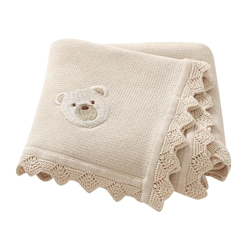Beige knitted baby blanket with a teddy bear applique on a white background