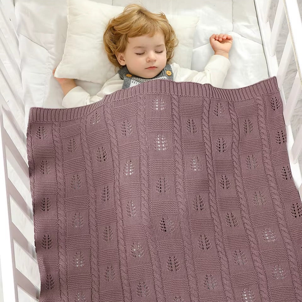 Child sleeping under a purple knitted blanket in a crib