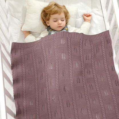 Child sleeping under a purple knitted blanket in a crib